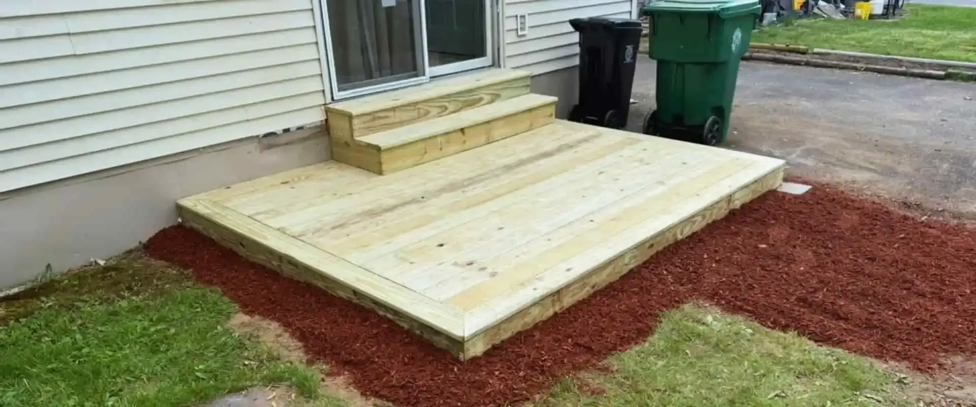 New wood floating deck with built-in box stairs and fresh mulch landscaping along the foundation