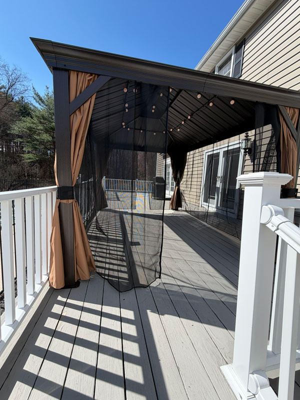 Metal gazebo installed on deck with curtains and lighting for outdoor shade and seating area
