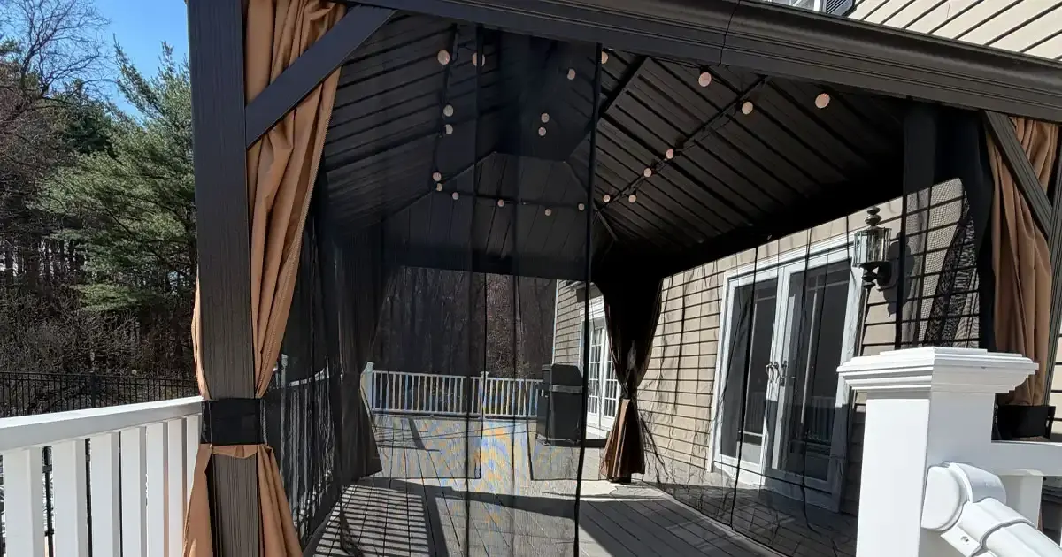 Metal-framed gazebo with mesh curtain walls and string lights installed on an existing deck