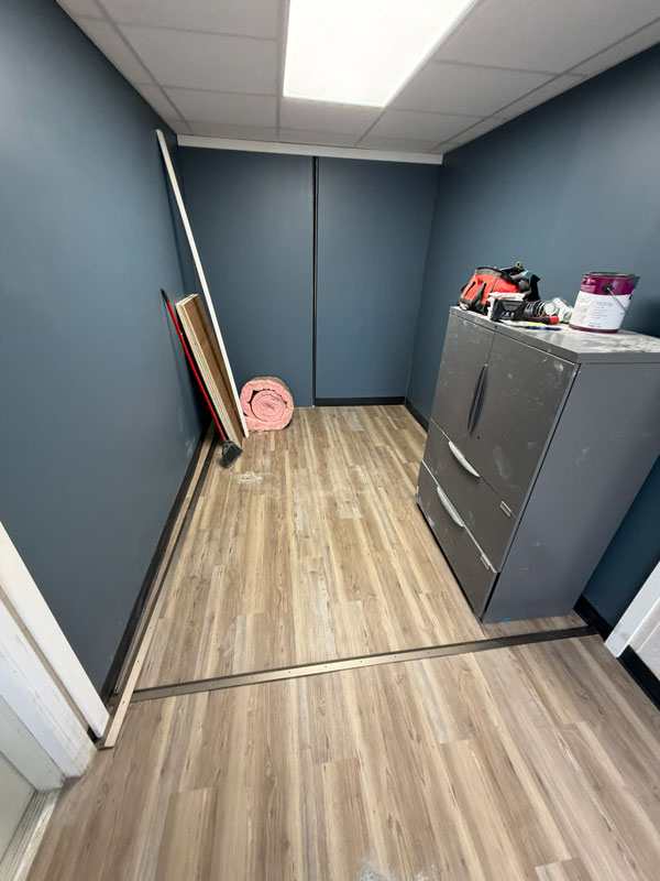 Finished interior of remodeled shipping container office with painted walls, flooring, and drop ceiling lighting