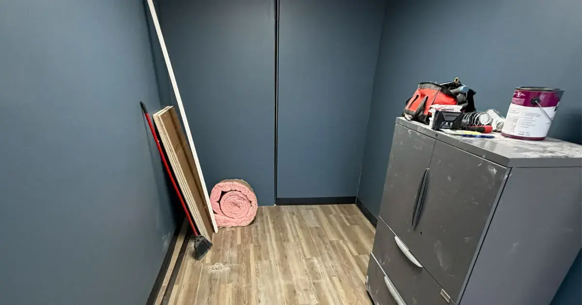 Interior of a shipping container mid-remodel with insulation and framing materials against blue walls