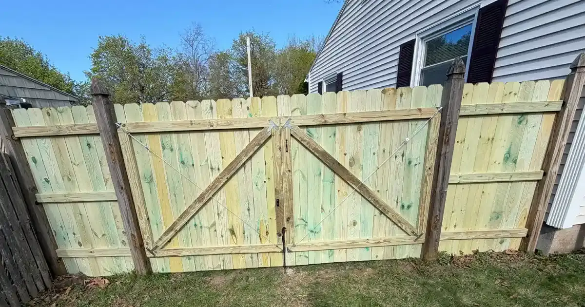 Pressure-treated wood dog-ear picket fence with a wide double gate installed in a backyard