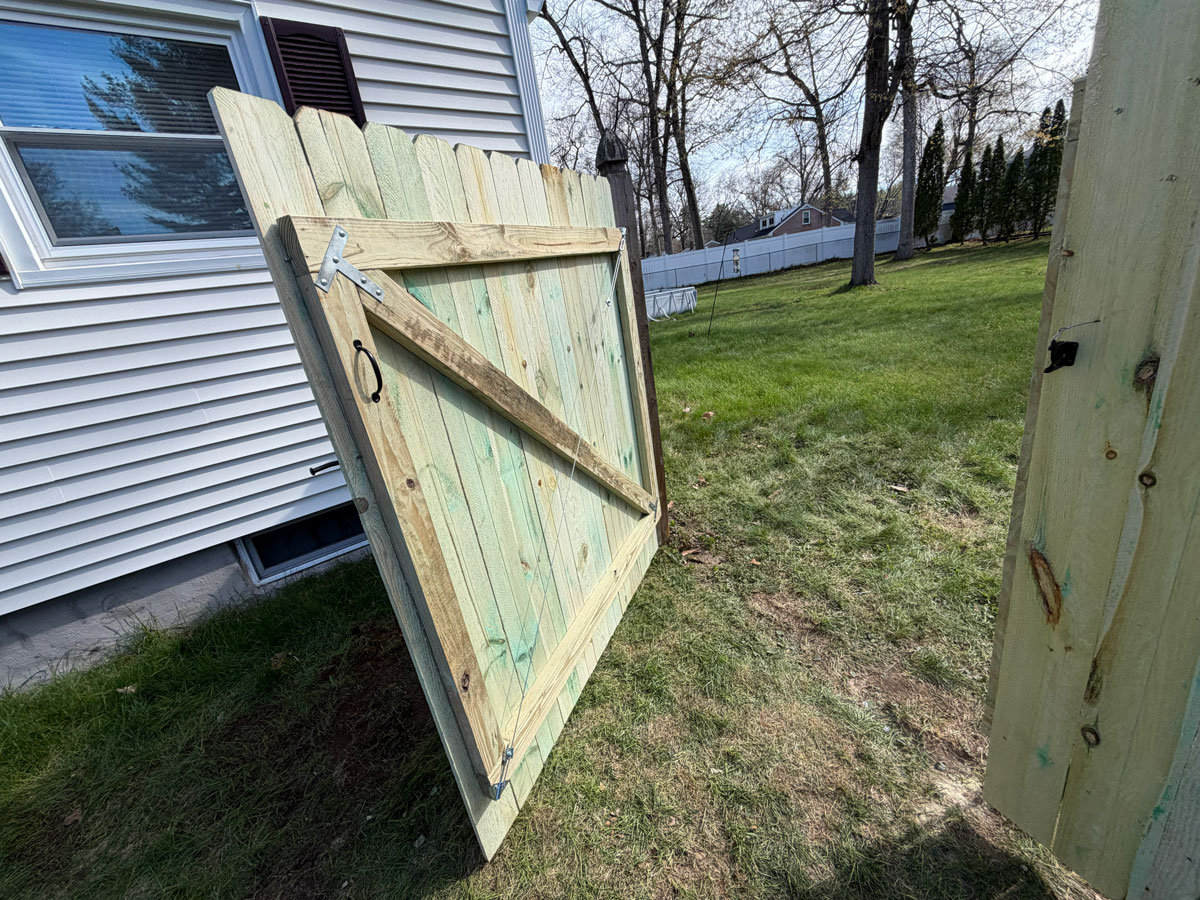 Pressure-treated wood fence gate with dog-ear pickets partially open showing hardware and framing
