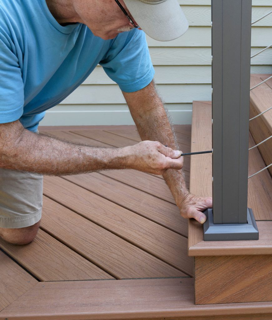Homeowner inspecting composite deck railing and stairs during summer deck maintenance