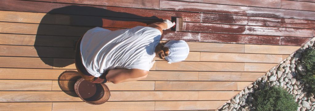 Applying deck stain and sealant to wood decking during summer deck maintenance