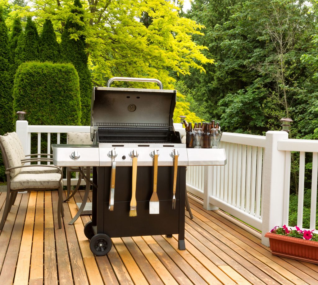 Backyard wood deck prepared for summer grilling with outdoor barbecue and white railing