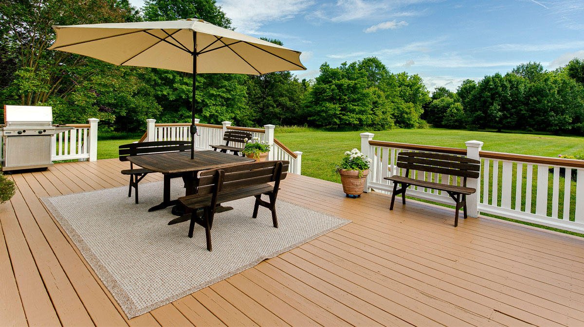 Large composite backyard deck prepared for summer with outdoor dining furniture, patio umbrella, and white railing