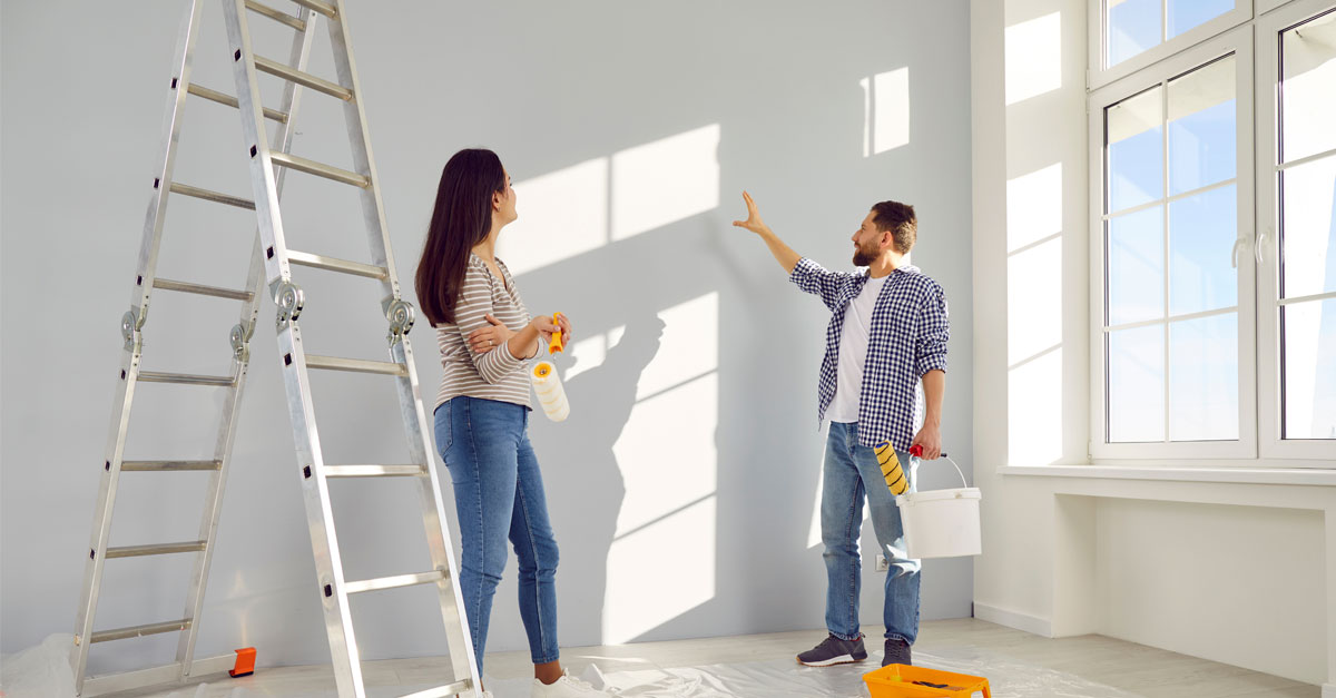 Homeowners preparing an interior painting project while evaluating wall colors in a bright room with natural sunlight