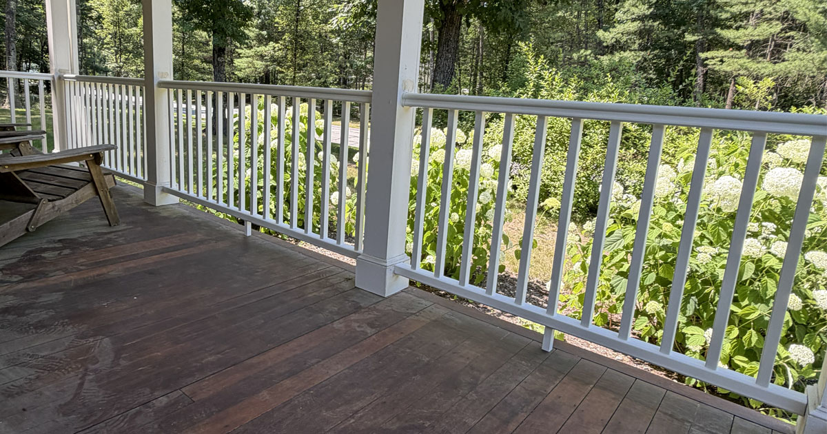 White vinyl porch railings installed along a covered front porch overlooking landscaped gardens