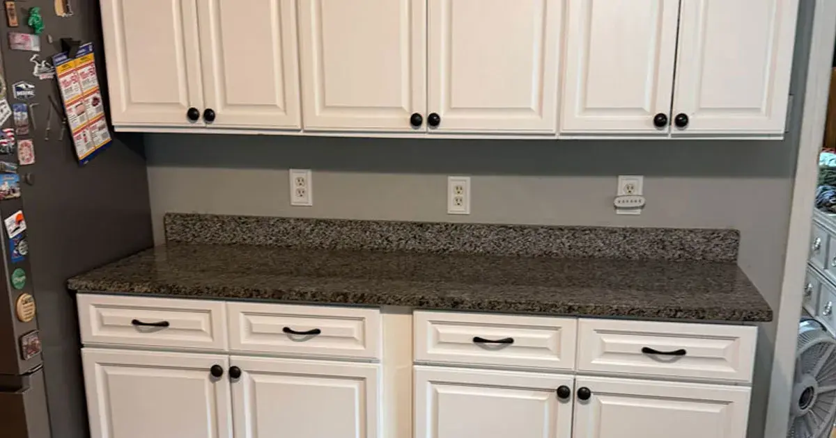 White kitchen cabinets installed above a dark granite countertop with black hardware