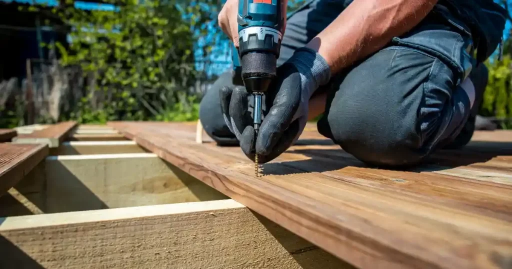 Contractor installing wood deck boards with a drill during custom deck construction on a residential outdoor deck frame.