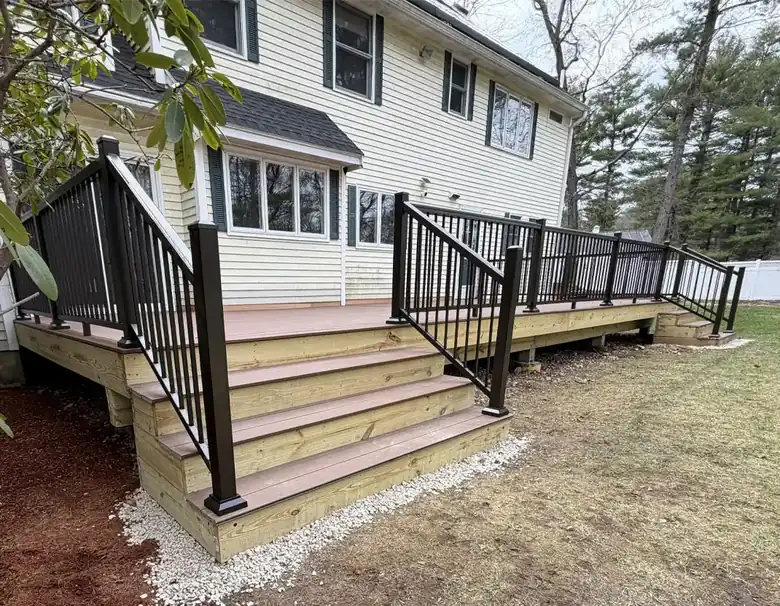 Composite backyard deck with black aluminum railings and wide stairs on a Massachusetts home