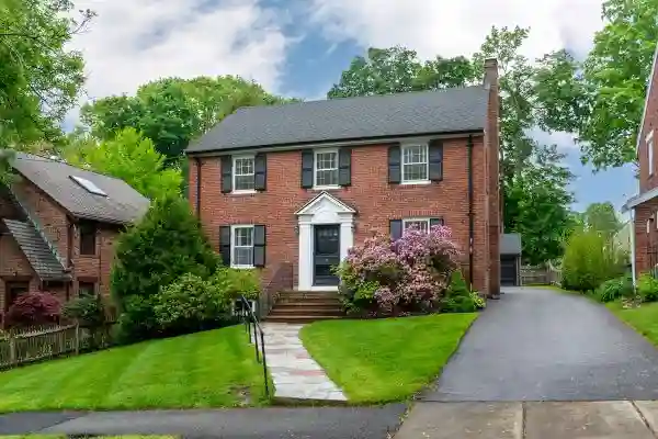 Brick colonial-style home with black shutters, white front door, and landscaped front yard, exterior view from the street.
