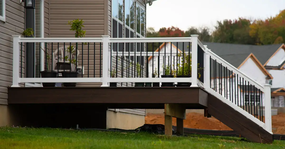 Composite deck with white PVC railings and staircase attached to a home exterior, elevated on support posts