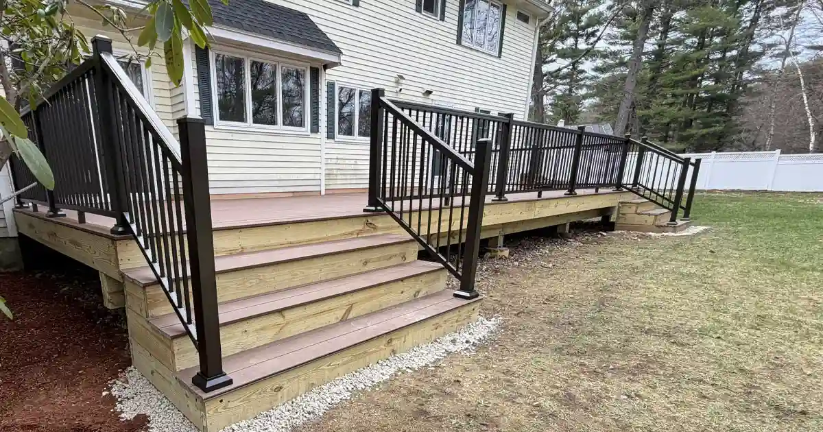 Custom wood deck with black metal railings, wide steps, and staircase built along a New England home