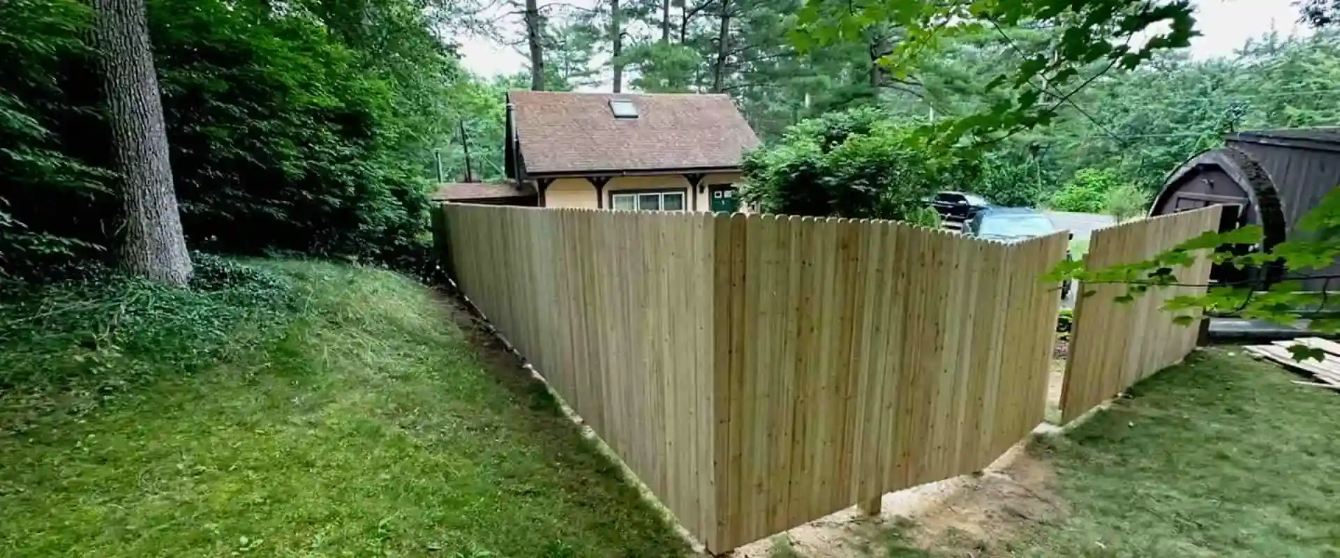 Wood picket privacy fence with a gate installed along a wooded backyard property line