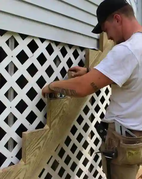 Contractor in tool belt installing a wood deck stair stringer against vinyl lattice skirting on a Cheshire County, NH home