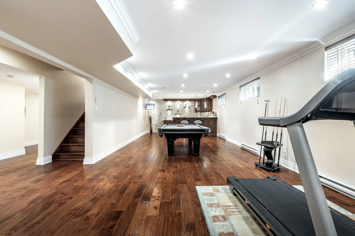 Finished basement with a pool table, wet bar, and treadmill on hardwood floors.