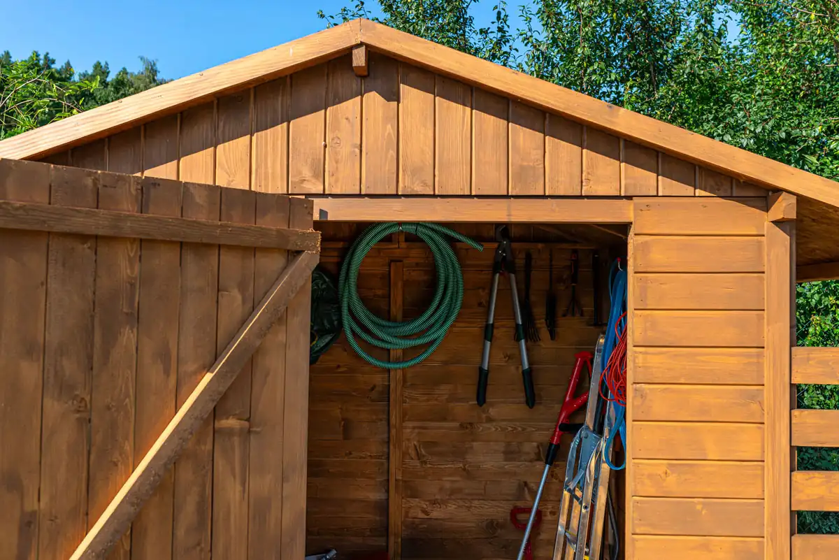 Open wooden garden shed with organized wall-mounted tools, shelving, and built-in storage for lawn equipment and outdoor supplies.