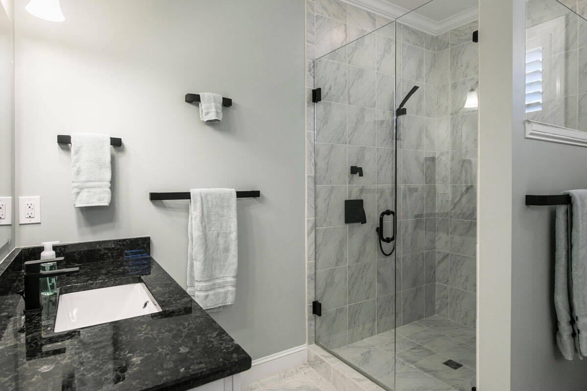 Modern bathroom remodel with a frameless glass walk-in shower, marble-look tile, black fixtures, and a quartz vanity.