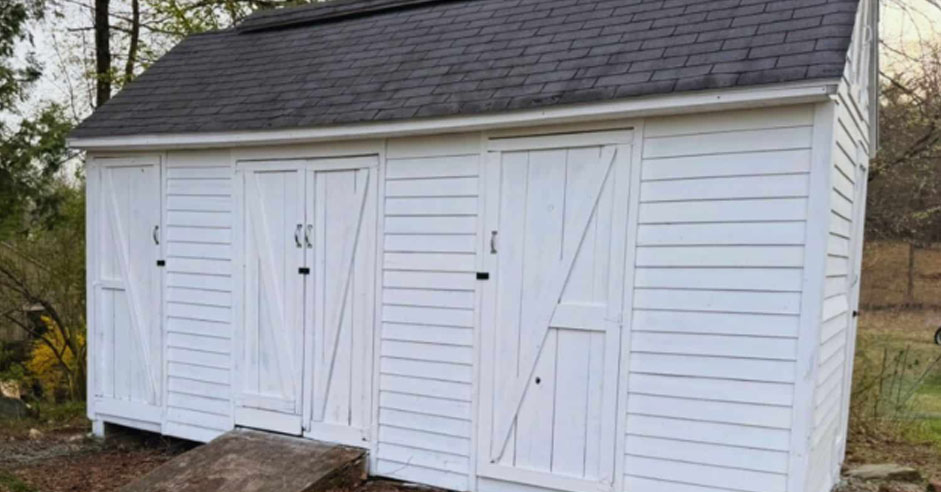 White storage shed with multiple barn-style doors, durable siding, and a shingled roof designed for organized outdoor storage and easy access.