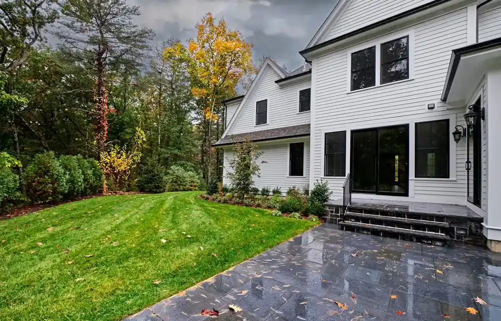 Remodeled white home with black-framed windows, stone patio, and landscaped backyard in Hampden County, MA