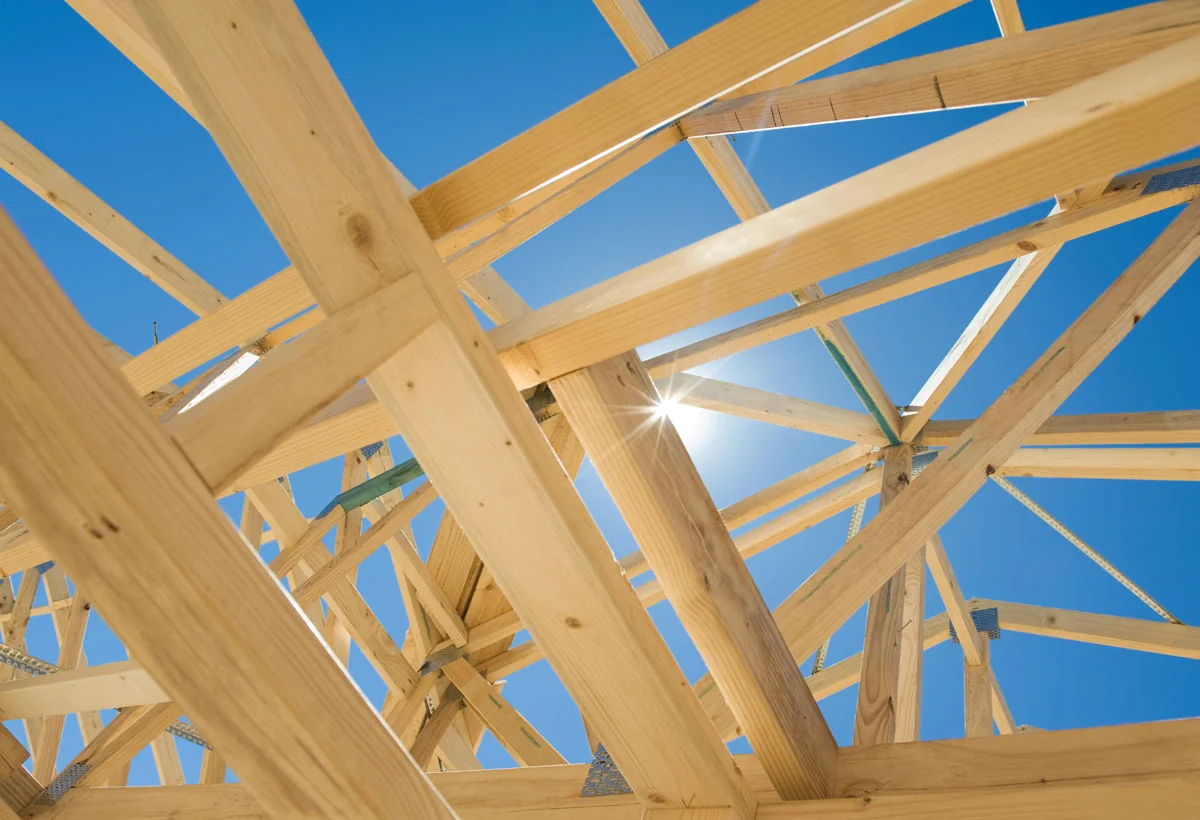Wood roof truss framing of a new home against a bright blue sky.