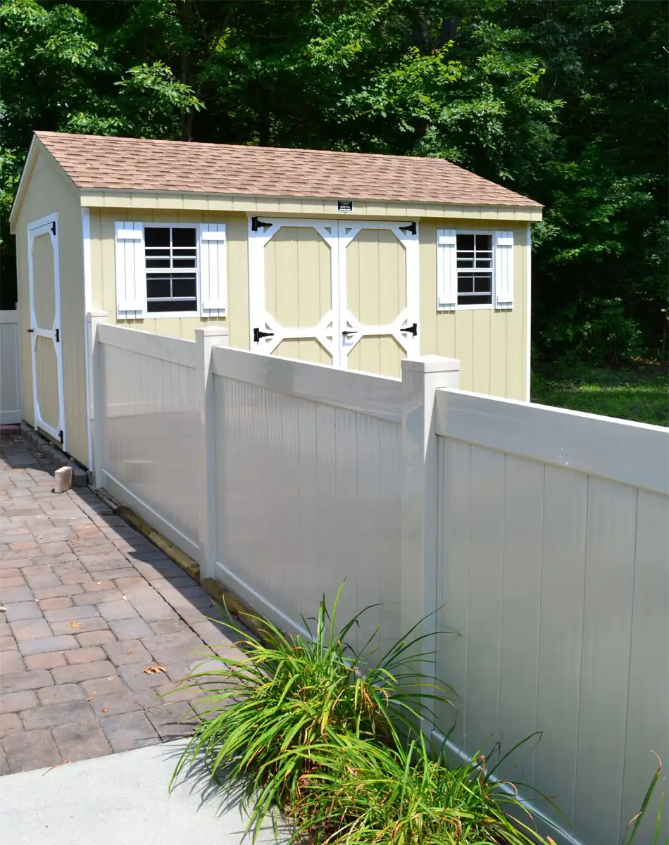 Custom backyard storage shed with double barn doors, windows, decorative shutters, and durable siding installed behind a white privacy fence.